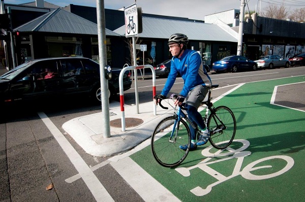 image of a bike rider stopped at the front of an intersection with a green and white painted bicycle box painted on the road.