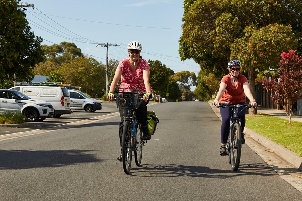 : two adults bike riding side by side, on a local street.