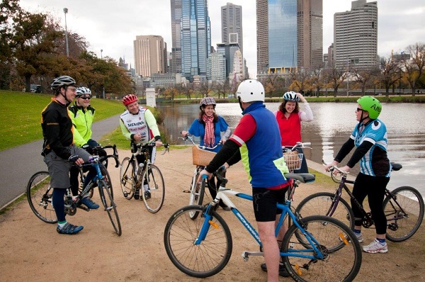 Image of a group of adult bike riders chatting to each other to the side of a shared path, with a view of the river and city.