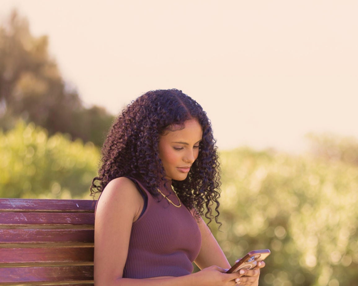 Young woman outdoors, holding a smartphone. Click to update your address and other details online.