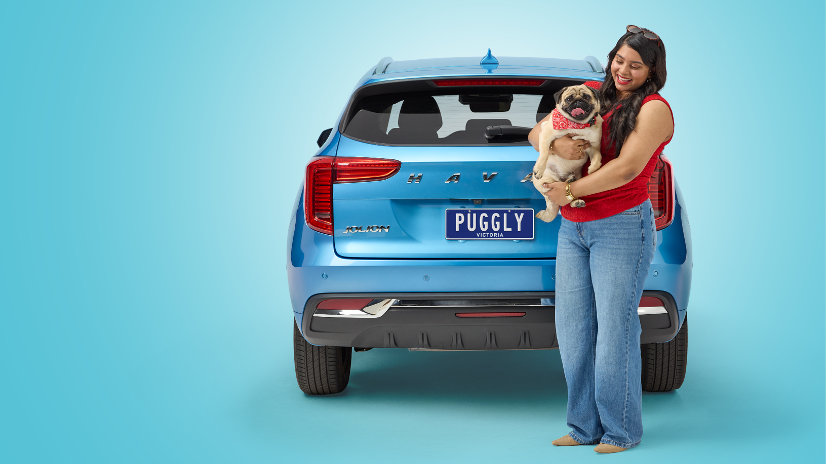 Woman with pug dog stands in front of blue car featuring the number plate 'Puggly'.