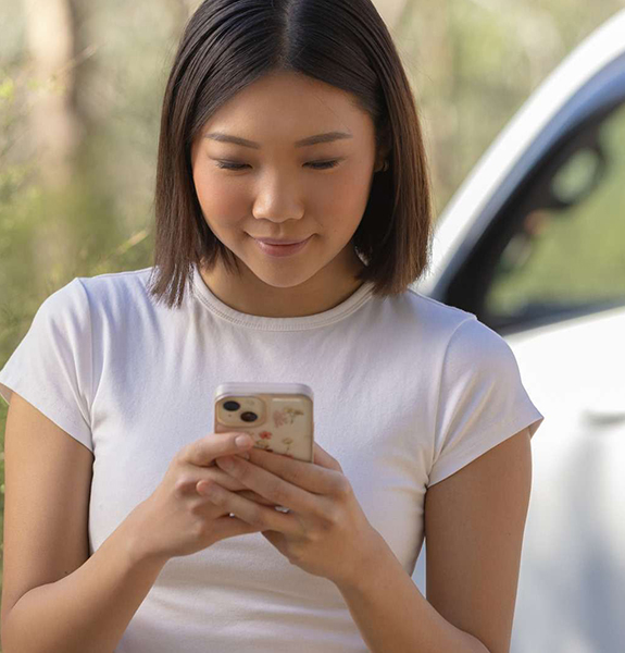 Young woman with phone standing beside car
