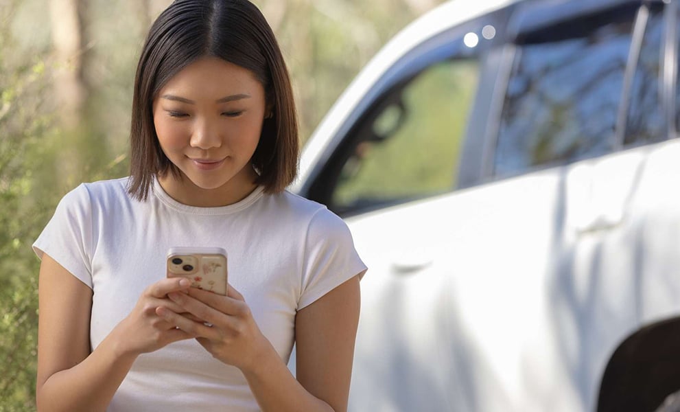 Young woman with phone standing beside car