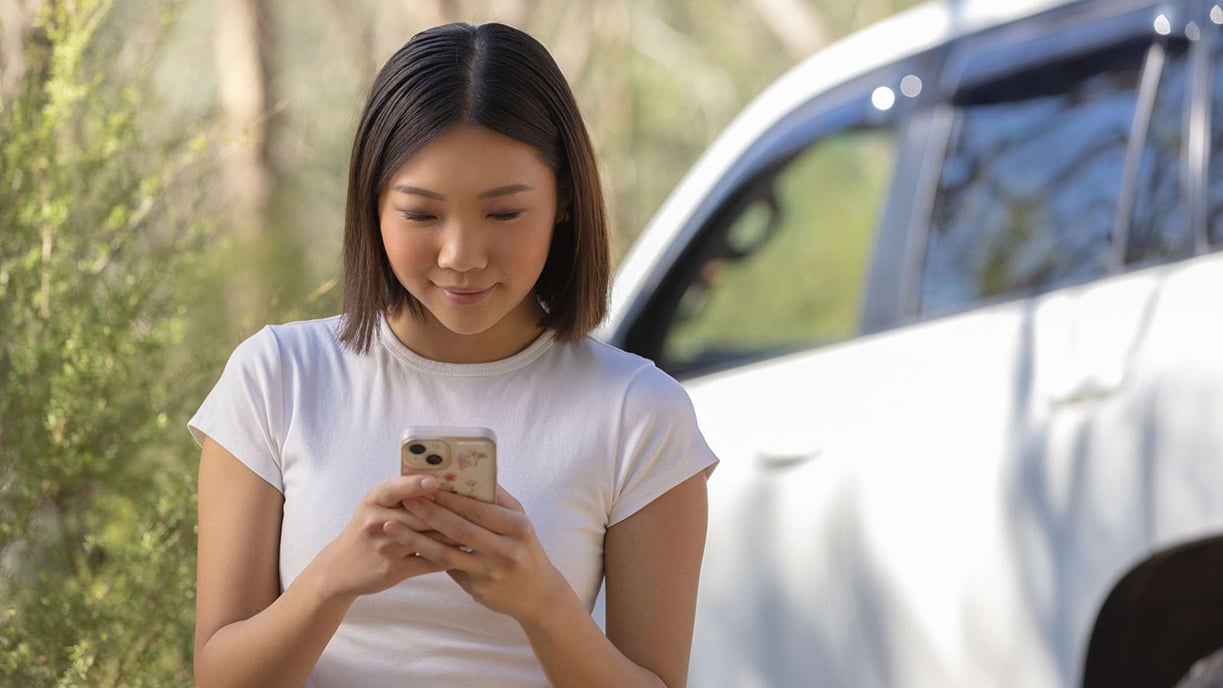 Young woman with phone standing beside car